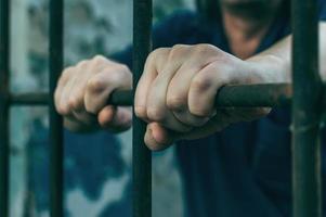 A depressed man in handcuffs behind bars. A depressed arrested male offender is jailed. Shouts, breaks, cries. photo