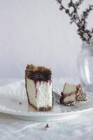 A slice of homemade cheesecake drizzled with currant jam and sprinkled with crumbs in a plate on a table covered with a white tablecloth. Selective focus. photo