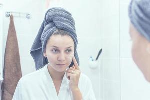 la niña en el baño frente al espejo con una toalla en la cabeza se aplica crema en la cara. enfoque selectivo. grano de la película