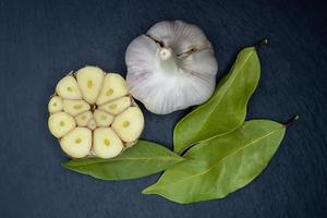 Top view of a whole garlic bulb, half a garlic bulb and bay leaves on a dark background. photo