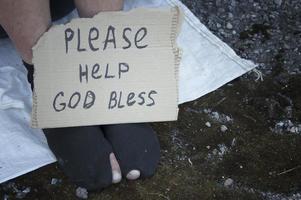 pies de un vagabundo sentado en la calle con calcetines rotos y un cartel con la inscripción. pobreza, desempleo, hambre.