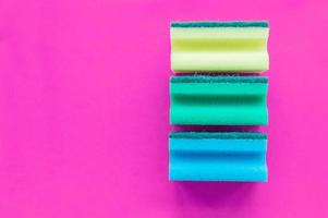 A stack of multicolored dishwashing sponges on a pink background with space for writing. photo
