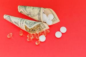 Medicines, vitamins and antioxidant supplements wrapped in money on a red background. The concept of expensive treatment.