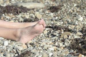 las piernas de la niña están arrugadas por el agua en una playa de guijarros bajo el sol. el concepto de turismo. foto