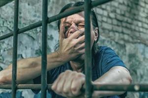 A depressed man holds his hands on the prison bars. Prisoner for the crime. Poor conditions. Scream, despair, pain, hunger. photo