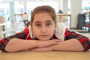 Teen girl is waiting for her order in a cafe. sitting at the table on the food court of the mall. shopping photo