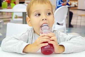 little child drinks juice sitting at a table on the food court of the mall. photo