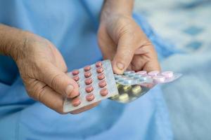 Asian senior woman patient holding antibiotics capsule pills in blister packaging for treatment infection patient in hospital, Pharmacy drugstore concept. photo