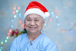 Paciente asiático mayor o mayor de la mujer de la señora mayor con el sombrero del ayudante de santa claus en la fiesta navideña del festival de la celebración de la Navidad y del año nuevo en el hospital. foto