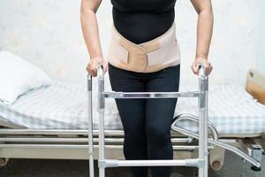 Asian lady patient wearing back pain support belt for orthopedic lumbar with walker. photo