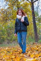 a portrait of a red - haired smiling girl in a jacket and scarf with her hair loose in full growth walks in the park . against the background of autumn nature, the concept of human emotion photo