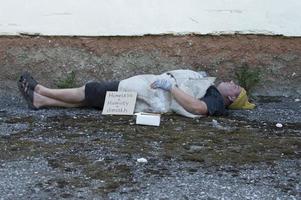 un vagabundo que está ebrio duerme en la calle con una botella de cerveza en la mano. pobreza, desempleo, alcoholismo. foto
