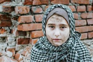 a refugee child in the war, a Muslim girl with a dirty face on the ruins, the concept of peace and war, the child is crying and waiting for help. photo