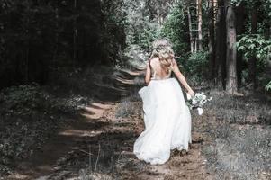 Beautiful bride blonde running through the woods alone. Wedding in the forest. photo