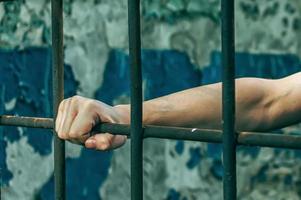 A depressed man in handcuffs behind bars. A depressed arrested male offender is jailed. Shouts, breaks, cries. photo