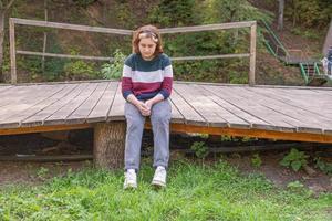 Una adolescente con un corte de pelo corto está sentada en un banco de madera largo en la naturaleza a principios de otoño foto