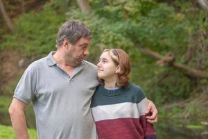 a teenage girl with her dad in nature look into each other's eyes against the background of green nature in early autumn photo