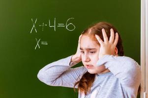 Schoolgirl solves a math problem on the blackboard during the lesson.