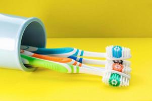 Multicolored toothbrushes in a blue glass on a yellow background. Close up. photo