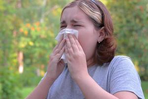 una niña con alergias en un parque de otoño. niña estornudando se suena la nariz en una servilleta y estornuda foto