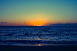 puesta de sol naranja en el mar y el cielo azul hermoso mar y puesta de sol con gran sol amarillo bajo las colinas de la superficie del mar en el fondo. foto
