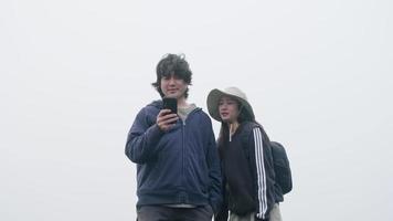 Pareja tomando fotos en la cima de la montaña con una espesa niebla de fondo video