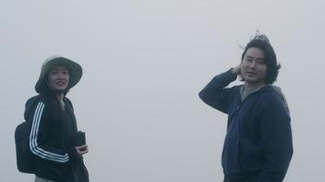 Couple taking photos on top of the mountain with thick fog in the background video