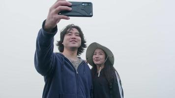 Couple taking photos on top of the mountain with thick fog in the background video