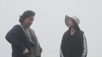 par som tar bilder på toppen av berget med tjock dimma i bakgrunden video