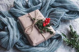 Caja de regalo junto al mantel vintage gris y hojas de abeto con frutos rojos sobre un fondo blanco. foto