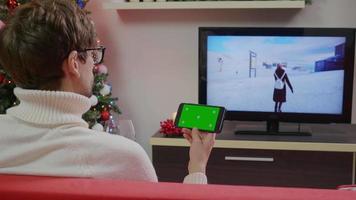 homem segurando smartphone com fundo de Natal chave croma de tela verde. video
