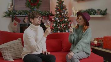 Happy couple clink wine glasses toast and celebrate together Christmas at home standing against Christmas tree. video