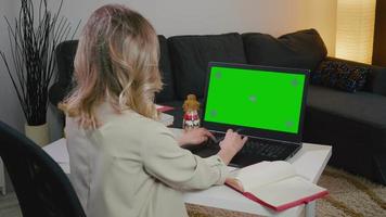 Woman makes notes and using laptop with green screen in home office. video