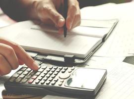 savings, finances, economy and home concept - close up of man with calculator counting making notes at home, hand is writes in a notebook with books, soft focus. photo