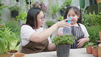 glückliche asiatische mutter, die ihrem kind beibringt, pflanzen durch sprühen zu pflegen und mit wasser einen kleinen baum in einem blumentopf zu besprühen. Familienaktivität am Wochenende. Gartengeräte