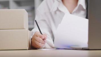 close-up hand vrouw die voorraad controleert, een notitie maakt en thuis op laptop typt om het belangrijkste document, online verkoopkanaal, thuis wakker te worden, dozen op tafel te zetten video