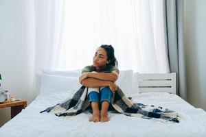 Sad African American woman wrapped herself in a blanket and looks to the side photo