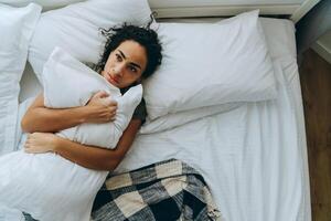 Overhead view of displeased African woman wrapped herself in a blanket and hugging pillow photo