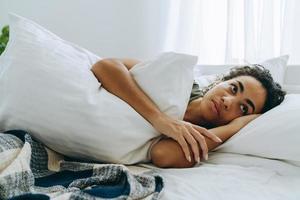 Pensive African woman wrapped herself in a blanket and hugging pillow photo