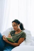 Mujer africana concentrada escribiendo algo en el bloc de notas en la cama foto