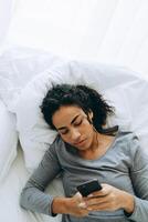 Young black woman using mobile phone while lying in her bed at home photo