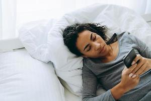 joven, mujer negra, utilizar, teléfono móvil, mientras, acostado, en cama