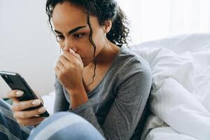 Joven mujer negra con teléfono móvil mientras está sentado en la cama foto