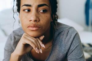 Joven mujer negra con el ceño fruncido y mirando a un lado mientras está sentado en la cama foto