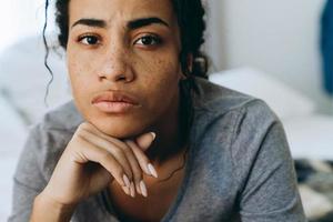 Young black woman frowning and looking at camera in bedroom