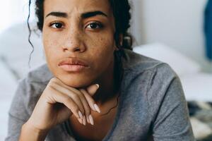 Young black woman frowning and looking at camera in bedroom photo