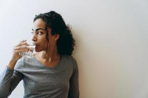 Joven mujer negra bebiendo agua durante pasar tiempo en casa foto