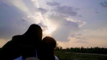 vista traseira da feliz mãe e filho asiáticos assistindo o maravilhoso pôr do sol e apontando para o céu deslumbrante, se divertindo com o pôr do sol à noite juntos e tendo uma conversa engraçada