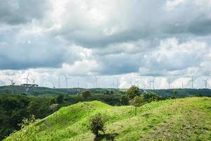 Aerogenerador de energía renovable en el paisaje de montaña con poste de alta tensión y poste eléctrico en colinas foto
