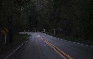 Road on the dark view on the mountain road among green forest trees - curve asphalt road lonely scary at night photo